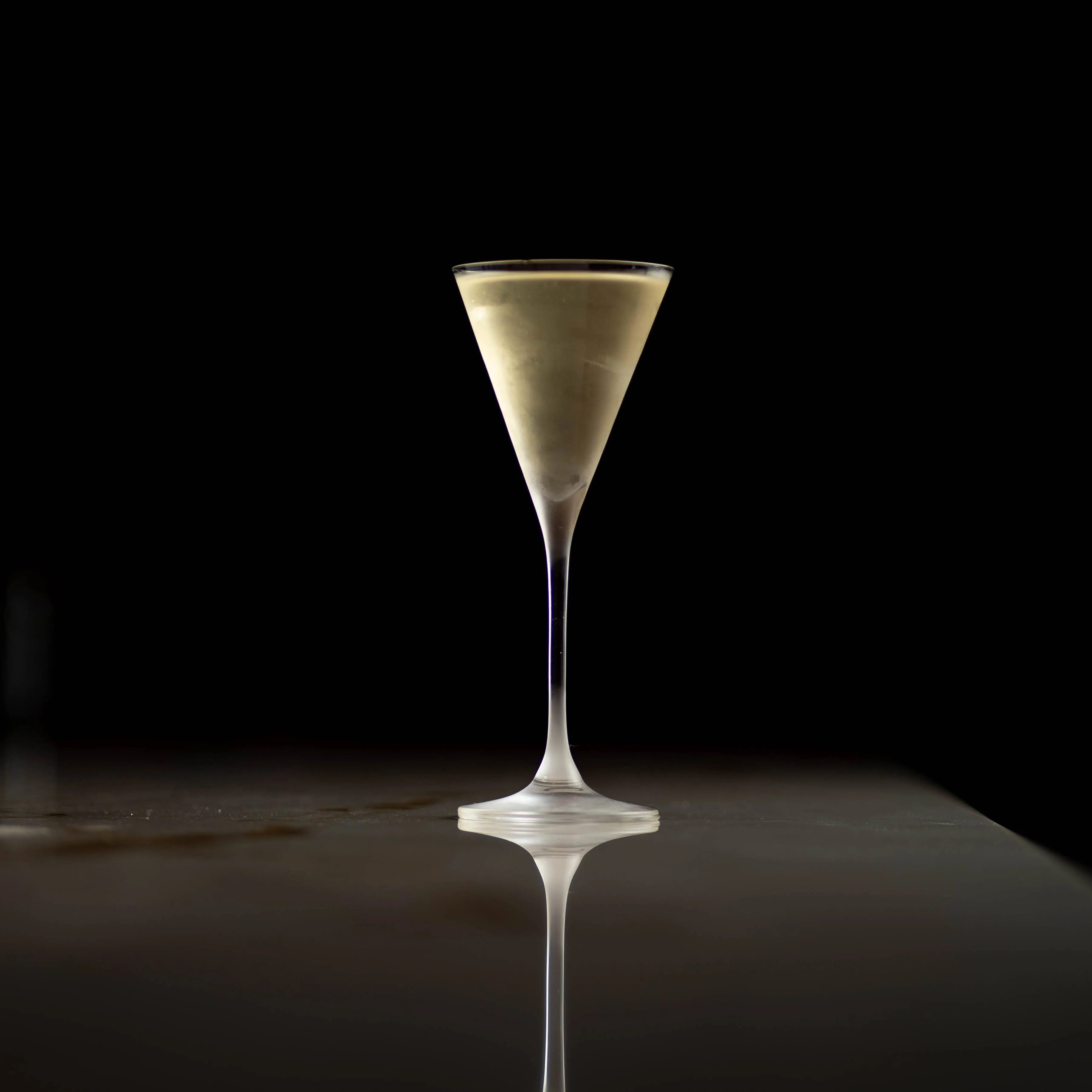 Martiniglass med klar cocktail mot svart bakgrunn