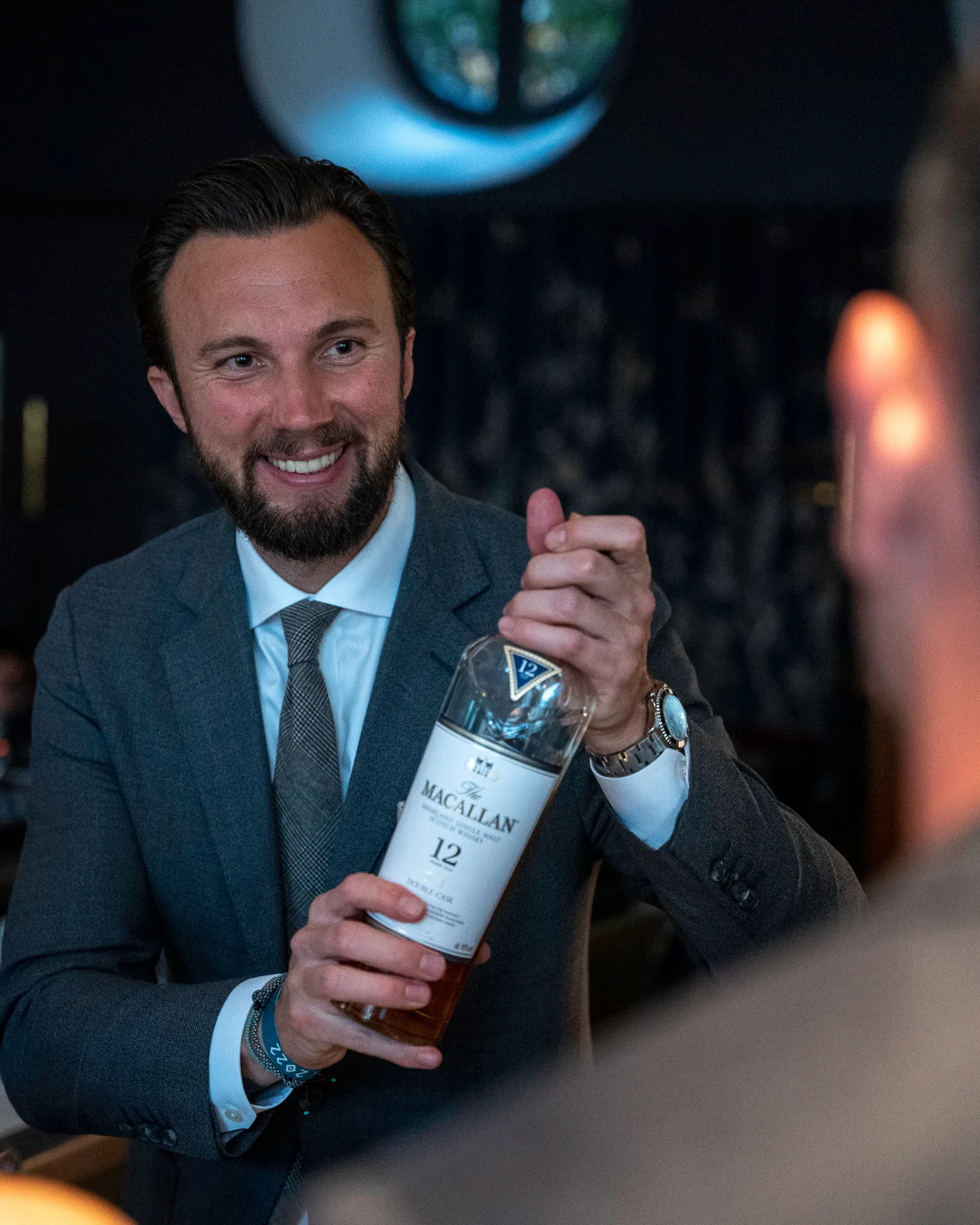 Mann i dress smiler og holder en flaske The Macallan 12