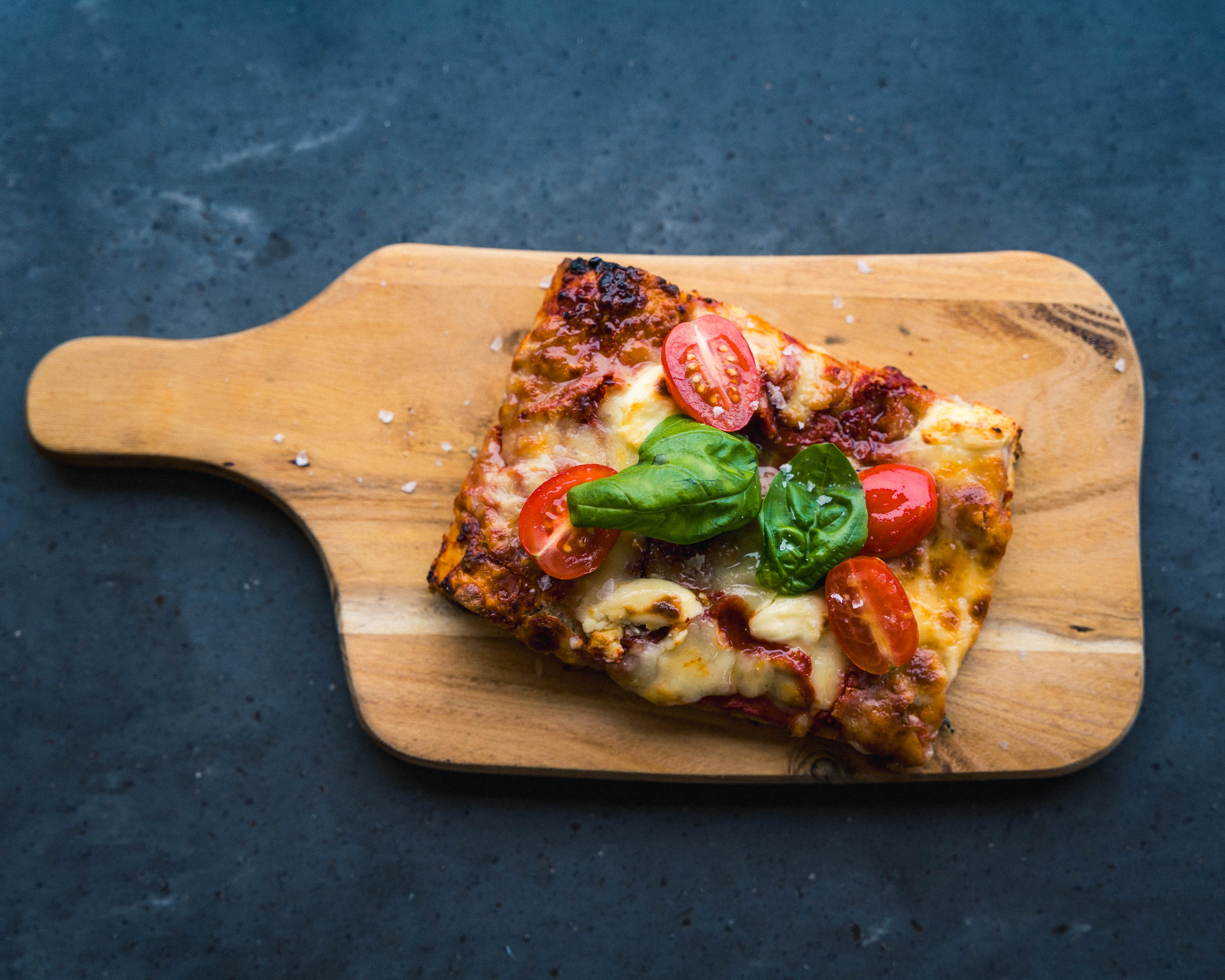 Pizzastykke med tomat og basilikum på et skjærebrett, sett ovenfra