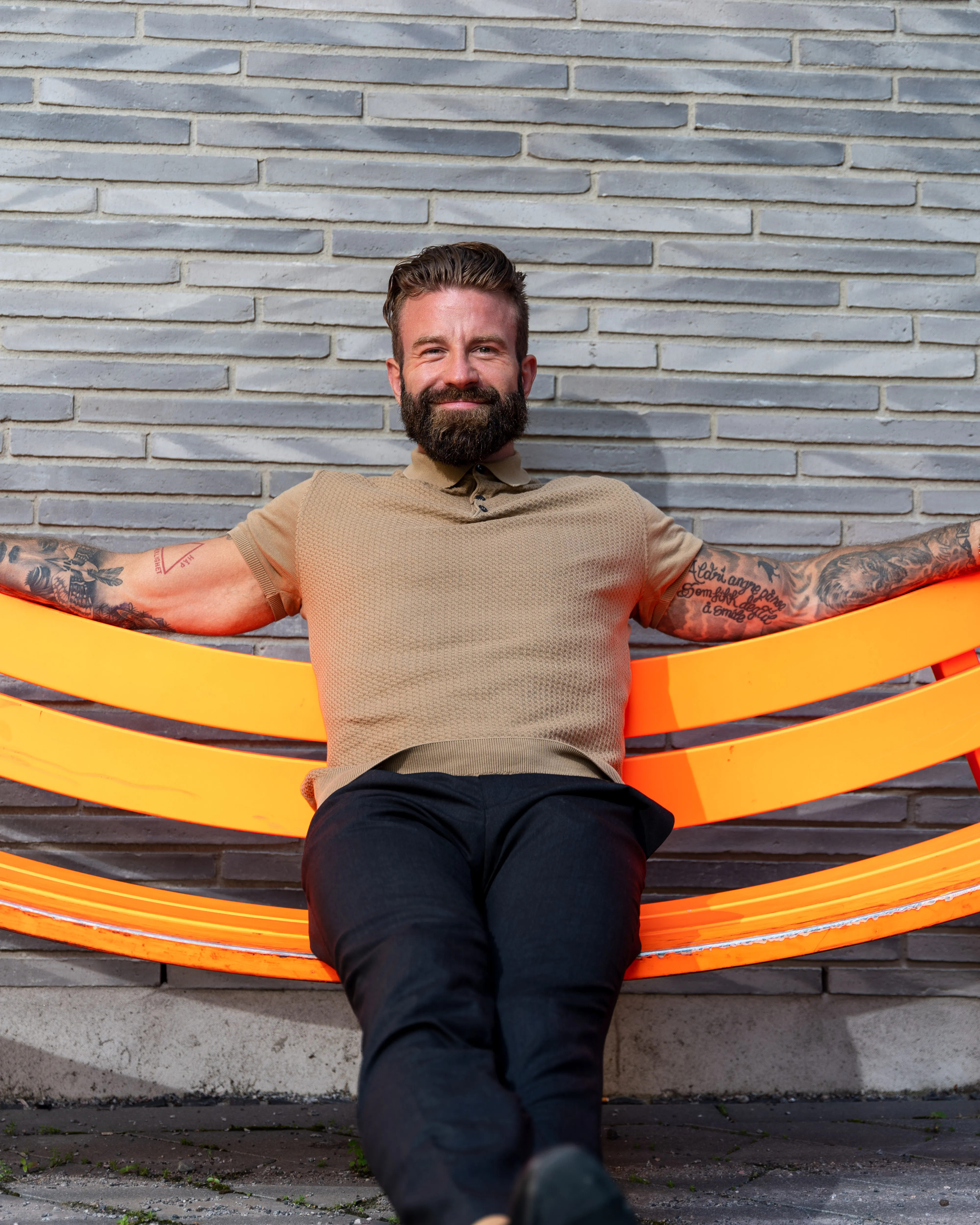 Aleksander Stormskjold lener seg tilbake på en oransje benk