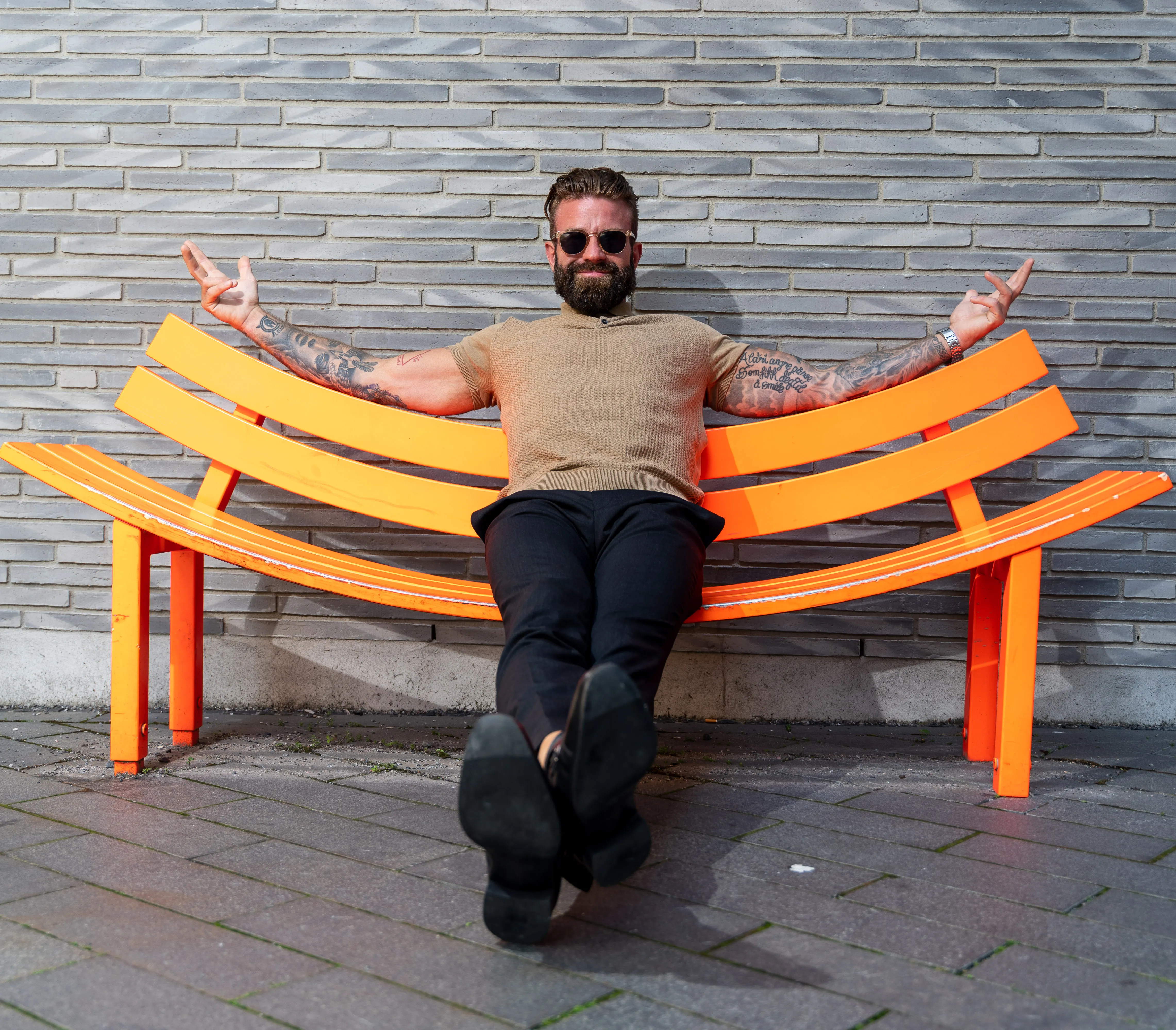 Aleksander Stormskjold med solbriller og armene ut på en oransje benk